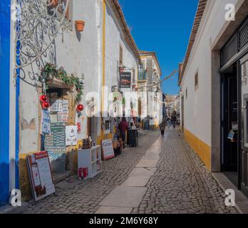 Blick auf die engen kopfsteingepflasterten Straßen des Obidos Viertels mit bunten Häusern, winzigen Geschäften und Cafés, die zu Weihnachten dekoriert sind. Stockfoto
