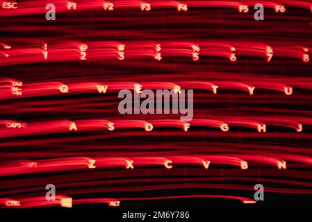 Leicht gemalte Buchstaben und Zahlen auf der Tastatur. Wunderschöner, farbenfroher Hintergrund. Lichtermalerei mit langer Belichtung, rote gekrümmte Linien in leuchtendem Neon. Stockfoto