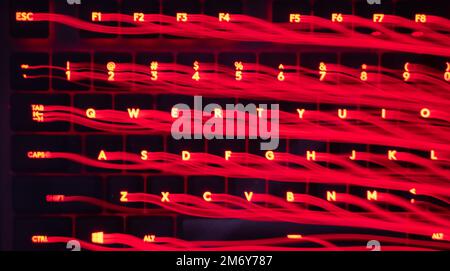 Leicht gemalte Buchstaben und Zahlen auf der Tastatur. Wunderschöner, farbenfroher Hintergrund. Lichtermalerei mit langer Belichtung, rote gekrümmte Linien in leuchtendem Neon. Stockfoto