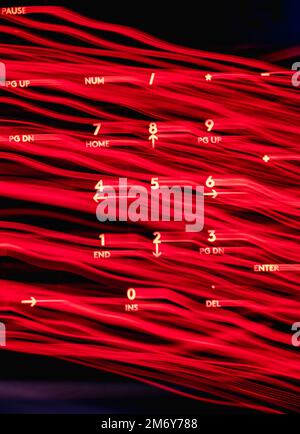 Helle Malerei auf Tastaturbuchstaben. Wunderschöner, farbenfroher Hintergrund. Lichtermalerei mit langer Belichtung. Rote gekrümmte Linien in leuchtendem Neon auf schwarzem Hintergrund. Stockfoto