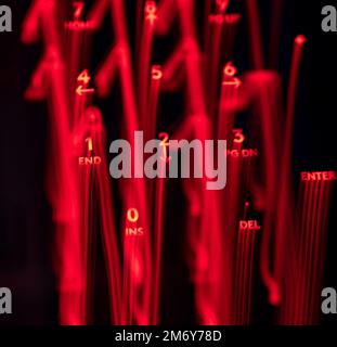 Helle Malerei auf Tastaturbuchstaben. Wunderschöner, farbenfroher Hintergrund. Lichtermalerei mit langer Belichtung. Rote gekrümmte Linien in leuchtendem Neon auf schwarzem Hintergrund. Stockfoto