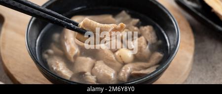 Four Tonics Suppe. Köstliches hausgemachtes taiwanesisches traditionelles chinesisches Kräutergericht mit Kräutern, Schweinedärm auf grauem Tischhintergrund Stockfoto