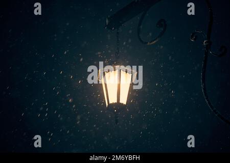 Alte Laterne mit gelbem Glanz bei nächtlichen Schneestürmen im Winter, Kopierraum auf verschwommenen Schneeflocken. Helles gelbes Licht aus antiker Laterne Stockfoto