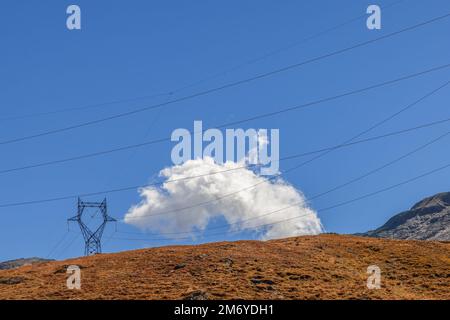 Divergierende Drähte der Hochspannungsleitung mit Masten auf Granithängen, die mit Herbstgras vor blauem Himmel bedeckt sind Stockfoto