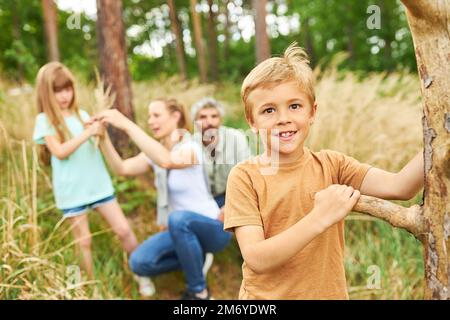 Porträt eines lächelnden Jungen, der Holz sammelt, während er mit der Familie im Wald im Urlaub campen geht Stockfoto