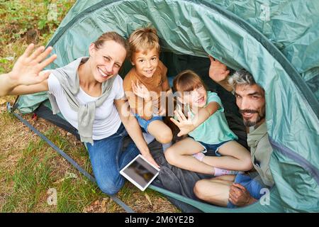 Hochwinkelporträt einer fröhlichen Familie, die während der Sommerferien im Zelt mit der Hand winkt Stockfoto