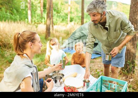 Mann und Frau, die sich unterhalten, während Kinder im Wald frühstücken, während sie campen Stockfoto