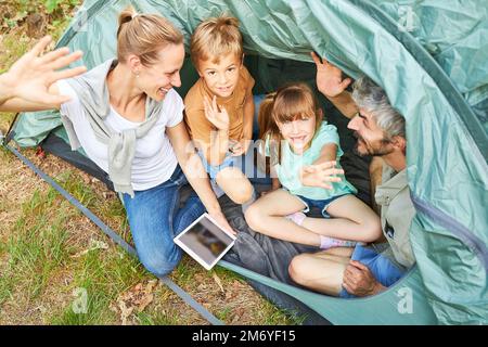 Blick aus einem hohen Winkel auf die glückliche Familie, die während der Sommerferien im Zelt mit der Hand winkt Stockfoto