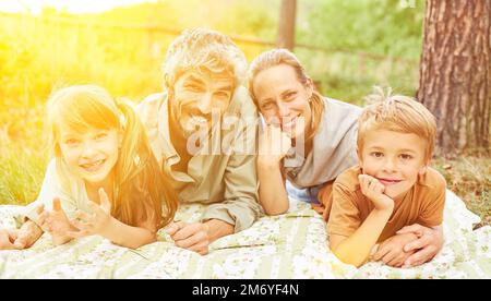 Lächelnde Familie mit zwei Kindern, die im Sommer im Park in der Natur liegen Stockfoto