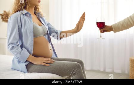 Junge schwangere Frau weigert sich Alkohol zu trinken und zeigt Stopp-Geste vor einem Glas Rotwein. Stockfoto