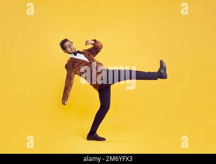 Fröhlicher, exzentrischer und lustiger junger, dunkelhäutiger Mann in Leopardenjacke isoliert auf gelbem Hintergrund. Stockfoto