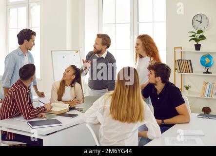 Kreativ-freundlicher männlicher Lehrer spricht und diskutiert mit Schülern, die Unterricht nehmen. Stockfoto