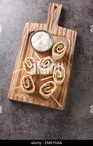 Norwegische Rolle mit geräuchertem Lachs, Frischkäse und Kräutern, in flaches Brot eingewickelt, Nahaufnahme auf einem Holzbrett auf dem Tisch. Vertikale Draufsicht von oben Stockfoto