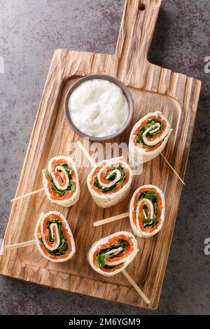 Lefserull med Rokelaks ist ein beliebtes norwegisches Gericht, bestehend aus geräuchertem Lachs, Frischkäse und Kräutern, die in flaches Brot eingewickelt sind, das auf dem Brett aufgemacht ist Stockfoto