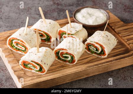 Dünne Pfannkuchen mit geräuchertem Lachs, Frischkäse und Rucola auf dem Brett auf dem Tisch. Horizontal Stockfoto