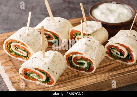 Vorspeise aus eingewickeltem geräuchertem Lachsfilet, Frischkäse und Kräutern in einer flachen Brotaufnahme auf einem Holzbrett auf dem Tisch. Horizontal Stockfoto