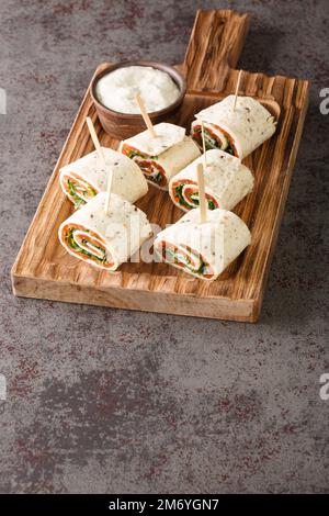 Norwegische Rolle mit geräuchertem Lachs, Frischkäse und Kräutern, in flaches Brot eingewickelt, Nahaufnahme auf einem Holzbrett auf dem Tisch. Vertikal Stockfoto