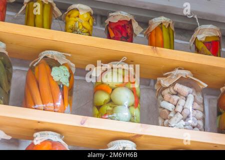 Eingelegtes Gemüse, trockener Kaffee, Flaschenverschlüsse in Glasgefäßen auf Regalen Stockfoto