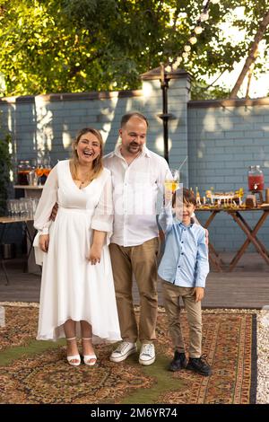 Porträt einer dreiköpfigen Familie mit Eltern, die heiraten, und ihrem süßen kleinen Sohn, der auf die Hochzeit anstoßen und im Hintergrund gequatscht und roman genießt Stockfoto