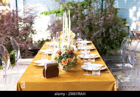 Hochzeit. Bankett. Stühle und ein Tisch für Gäste, dekoriert mit Kerzen, werden mit Besteck und Geschirr serviert und mit gelber Tischdecke bedeckt. Die Stockfoto