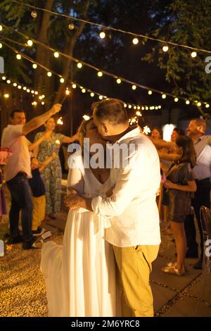 Bräutigam, Braut und Hochzeitsgäste mit brennenden Lichtern im Freien auf einer Cocktailparty. Glück, Feiern und Liebeskonzept Stockfoto