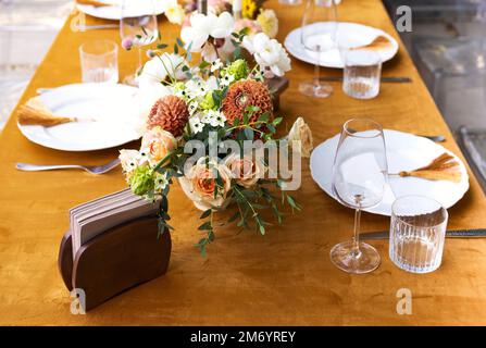 Hochzeit. Bankett. Stühle und ein Tisch für Gäste, dekoriert mit Kerzen, werden mit Besteck und Geschirr serviert und mit gelber Tischdecke bedeckt. Die Stockfoto