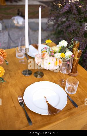 Hochzeit. Bankett. Stühle und ein Tisch für Gäste, dekoriert mit Kerzen, werden mit Besteck und Geschirr serviert und mit gelber Tischdecke bedeckt. Die Stockfoto