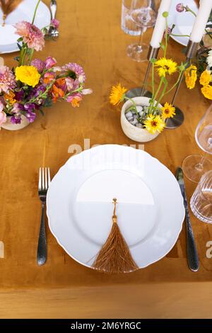 Hochzeit. Bankett. Stühle und ein Tisch für Gäste, dekoriert mit Kerzen, werden mit Besteck und Geschirr serviert und mit gelber Tischdecke bedeckt. Die Stockfoto