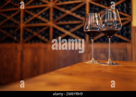 Verkostung. Weinflaschen auf einem Holzregal. Weinbar. Zwei Gläser mit Rotwein auf Holzhintergrund Stockfoto