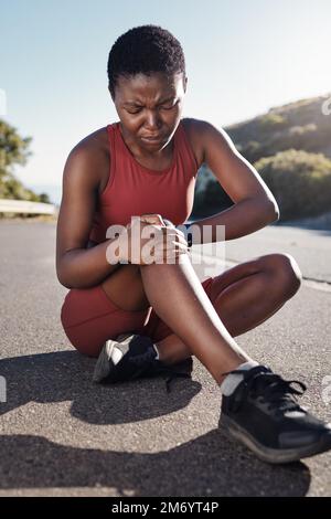 Schwarze Frau, Knie- und Sportverletzungen auf Asphalt bei Schmerzen durch Unfall, Sport oder Laufen im Freien. Afroamerikanische Frau mit Beinschmerzen Stockfoto