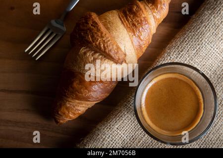 Croissant mit Espresso in weißer Tasse auf Holztisch Stockfoto
