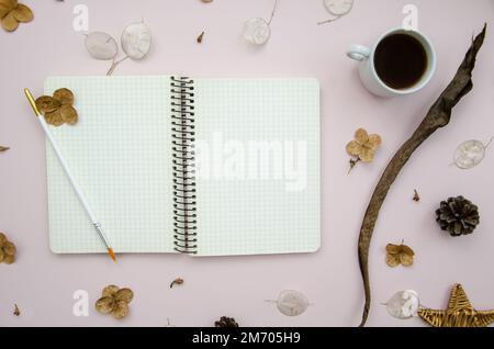 Urlaubskonzept. Craft Öko Geschenk, getrocknete Blumen, Lunaria Rediviva, Kaffeetasse, Tannenzapfen, Weidensterne, Kunstpinsel auf Rosenhintergrund. Notizbuch Stockfoto