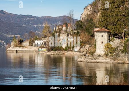 Castelveccana, Italien- 12-27-2022: Alte zerstörte Öfen mit Schornsteinen mit roten Ziegelsteinen, die auf dem Wasser des Lago Maggiore im Parco delle Fornac reflektieren Stockfoto