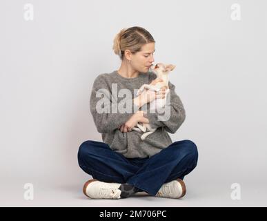 Junge Frau, die mit ihrem chihuahua Welpen auf dem Schoß sitzt Stockfoto