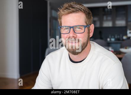 Nahaufnahme Porträt eines lächelnden 30s Weißen Mannes Betrachten Sie die Kamera und posieren Sie in der eigenen Wohnung oder Wohnung. Profilbild eines glücklichen 30s männlichen Mieters oder Mieters in n Stockfoto
