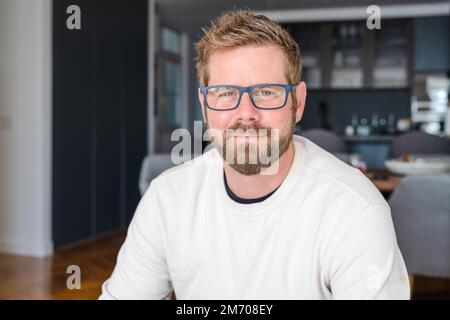 Ein junger, gutaussehender Mann mit Brille, der zu Hause lächelt. Stockfoto