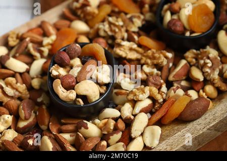 Mischen Sie Nüsse und getrocknete Früchte auf einem Holzbrett und in einer Schüssel. Gesunde Süßigkeiten. Stockfoto