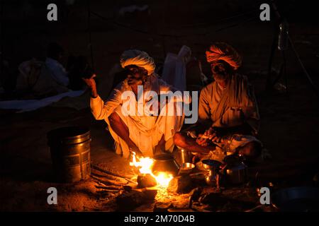 Pushkar, Indien - 6. November 2019: Indische Landdorfbewohner und Kamele, die nachts auf der Kamelmesse Pushkar Mela vom Lagerfeuer angezündet werden - jährlich berühmtes Ca Stockfoto