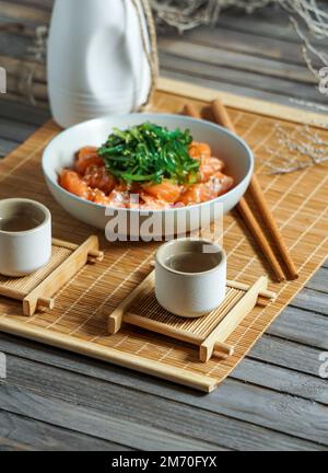 Japanischer Sake und Lachs-Sashimi und Wachalgen auf einer Bambusmatte Stockfoto