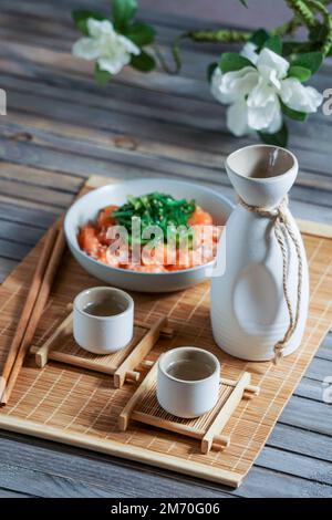 Japanischer Sake und Lachs-Sashimi und Wachalgen auf einer Bambusmatte Stockfoto