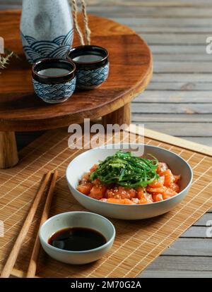 Japanischer Sake, Lachs, Sashimi und Algen auf asiatischem Holztisch Stockfoto