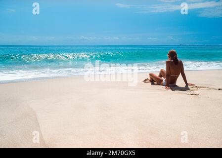 Tropischer Strandurlaub, Rückansicht einer jungen Frau, die allein an einem einsamen weißen Sandstrand sitzt und auf den Indischen Ozean, Tangalle, Sri Lanka blickt Stockfoto