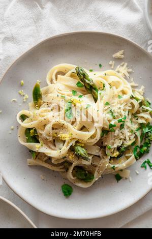 Zitronenpasta mit Spargel, veganem Käse und frischem Basilikum auf einem luftigen Tisch Stockfoto