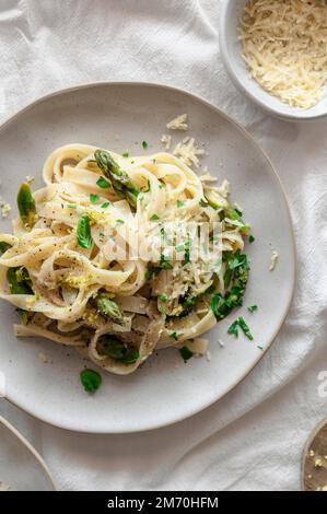 Zitronenpasta mit Spargel, veganem Käse und frischem Basilikum auf einem luftigen Tisch Stockfoto