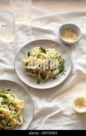 Zitronenpasta mit Spargel, veganem Käse und frischem Basilikum auf einem luftigen Tisch Stockfoto