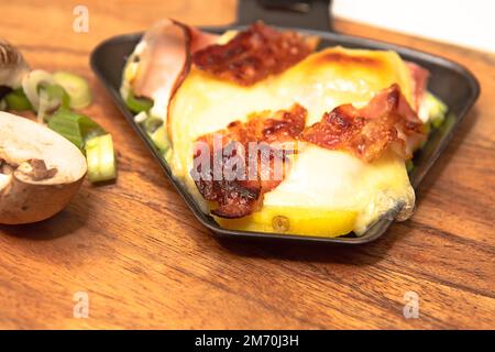 Raclette-Pfanne mit Käse und Speck Stockfoto