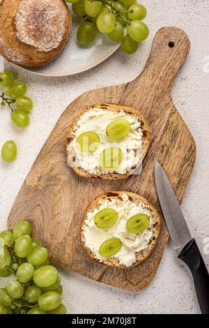 Zwei Sandwiches mit Frischkäse und Trauben auf einem Schneidebrett. Stockfoto