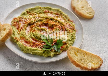 Avocado hummus gewürzt mit Sesam, Paprika und Petersilie. Das Gericht wird mit Toast serviert. Stockfoto