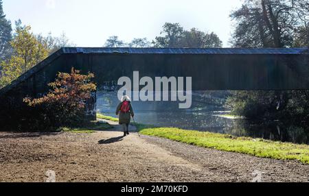 Eine alleinstehende Frau mittleren Alters, die an einem kalten und frostigen Wintertag in Surrey England UK am River Wey Navigationskanal in New Haw vorbeiläuft Stockfoto