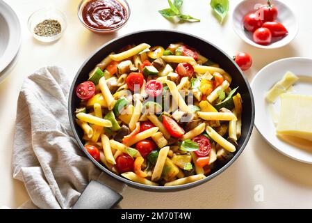 Penne Pasta mit geröstetem Gemüse in der Pfanne auf hellem Steinhintergrund. Stockfoto